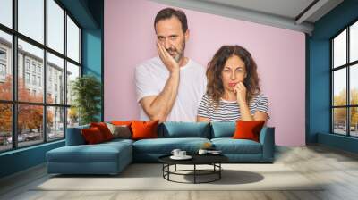 Beautiful middle age couple together standing over isolated pink background thinking looking tired and bored with depression problems with crossed arms. Wall mural