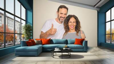 Beautiful middle age couple together standing over isolated white background doing happy thumbs up gesture with hand. Approving expression looking at the camera with showing success. Wall mural