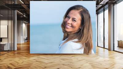 Beautiful middle age hispanic woman standing with smile on face at the ocean. Smiling confident and cheerful on a sunny day with sea view. . Wall mural