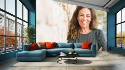 Beautiful middle age woman smiling cheerful leaning on a brick wall at the city street on a sunny day Wall mural