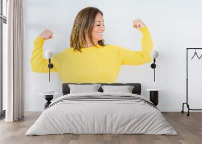 Beautiful middle age woman wearing yellow sweater over isolated background showing arms muscles smiling proud. Fitness concept. Wall mural