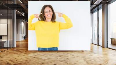 Beautiful middle age woman wearing yellow sweater over isolated background Smiling pointing to head with both hands finger, great idea or thought, good memory Wall mural