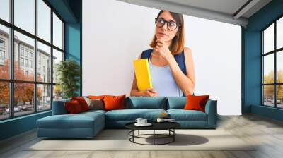 Beautiful redhead student woman wearing a backpack and book serious face thinking about question, very confused idea Wall mural