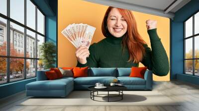 Beautiful redhead woman holding 5000 south korean won banknotes screaming proud, celebrating victory and success very excited with raised arm Wall mural