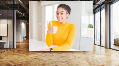 Beautiful young african american woman with afro hair doing happy thumbs up gesture with hand. Approving expression looking at the camera with showing success. Wall mural