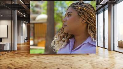 Beautiful young african american woman with braids in an outdoor urban park setting, looking thoughtful on a sunny day. Wall mural