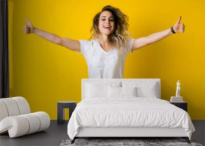 Beautiful young blonde woman jumping happy and excited with thumbs up over isolated yellow background Wall mural