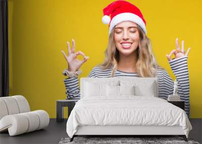 Beautiful young blonde woman wearing christmas hat over isolated background relax and smiling with eyes closed doing meditation gesture with fingers. Yoga concept. Wall mural