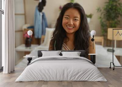 Beautiful young chinese woman smiling while sitting on a bed in a cozy bedroom in china with soft natural light and stylish decor. Wall mural