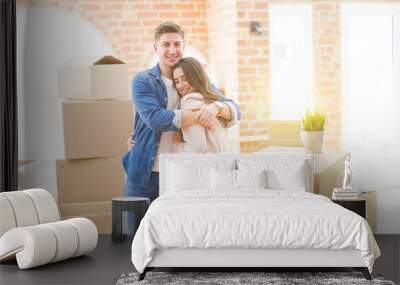 Beautiful young couple moving to a new home, standing on new aparment around cardboard boxes, hugging smiling happy and in love Wall mural