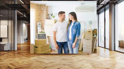 Beautiful young couple moving to a new house, smiling happy arround cardboard boxes Wall mural