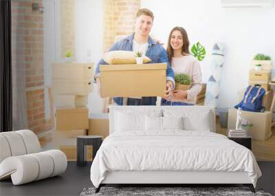 Beautiful young couple smiling in love holding cardboard boxes, happy for moving to a new home Wall mural