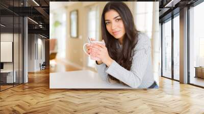 Beautiful young girl drinking a cup of coffee at home and smiling Wall mural