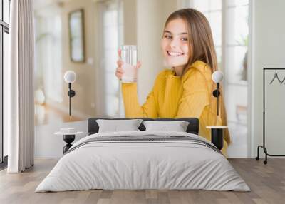 Beautiful young girl kid drinking a fresh glass of water with a happy face standing and smiling with a confident smile showing teeth Wall mural