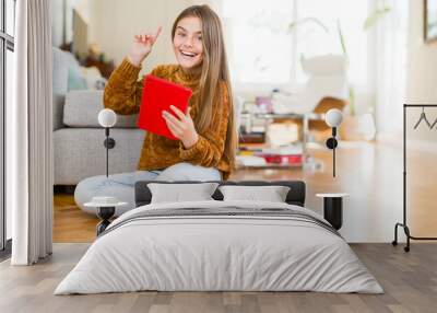 Beautiful young girl kid using digital touchpad tablet sitting on the floor surprised with an idea or question pointing finger with happy face, number one Wall mural