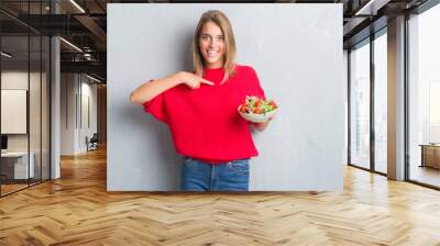 Beautiful young woman over grunge grey wall eating tomato salad with surprise face pointing finger to himself Wall mural