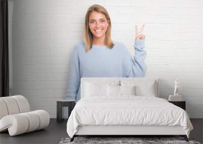 Beautiful young woman over white brick wall showing and pointing up with fingers number two while smiling confident and happy. Wall mural