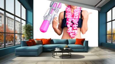 Beautiful young woman with short hair wearing bikini and hawaiian lei holding water gun pointing thumb up to the side smiling happy with open mouth Wall mural