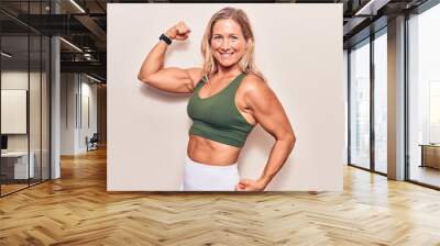 Blonde caucasian middle age sports woman posing and showing arms strength over isolated background Wall mural