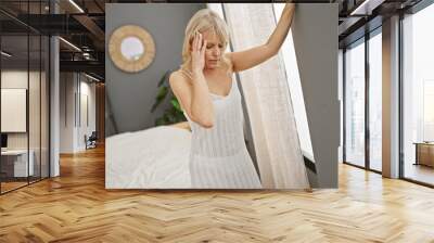 Blonde woman feeling dizzy in a modern bedroom with neutral colors and indoor plants. Wall mural