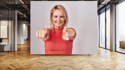 Blonde woman standing over isolated background pointing to you and the camera with fingers, smiling positive and cheerful Wall mural