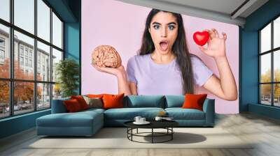 Brunette teenager girl holding brain and heart afraid and shocked with surprise and amazed expression, fear and excited face. Wall mural