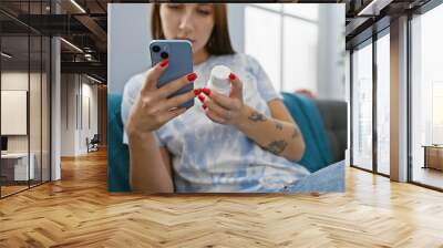 Brunette woman examines pill bottle while holding smartphone in a modern living room Wall mural