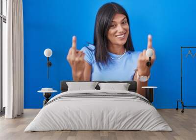 Brunette young woman standing over blue background showing middle finger doing fuck you bad expression, provocation and rude attitude. screaming excited Wall mural