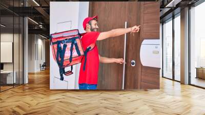 Caucasian delivery man wearing red uniform and delivery backpack smilly happy outdoors Wall mural