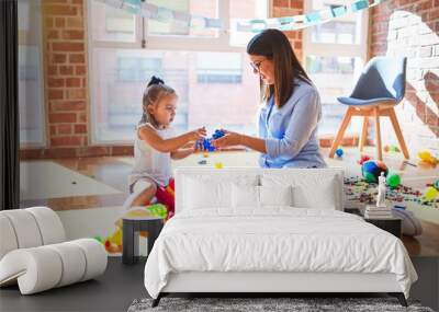 Caucasian girl kid playing and learning at playschool with female teacher. Mother and daughter at playroom around toys playing with bulding blocks Wall mural