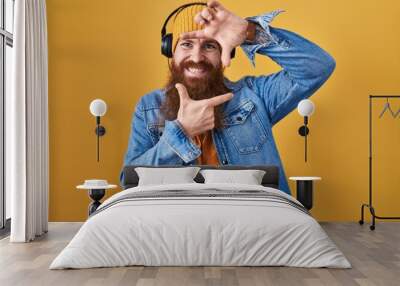 Caucasian man with long beard listening to music using headphones smiling making frame with hands and fingers with happy face. creativity and photography concept. Wall mural