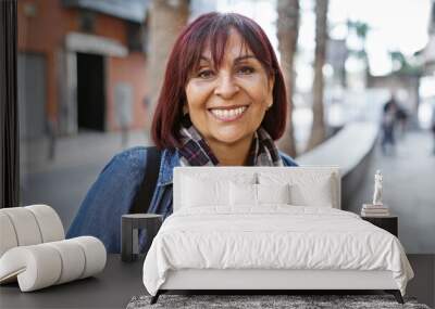 Confident middle-aged hispanic woman smiling in a city street, portraying everyday urban life. Wall mural