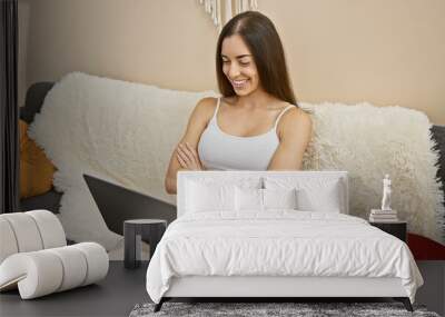 Confident young hispanic woman, relaxing on her sofa, arms crossed with a big smile while making a positive financial move using her laptop and credit card at home. Wall mural