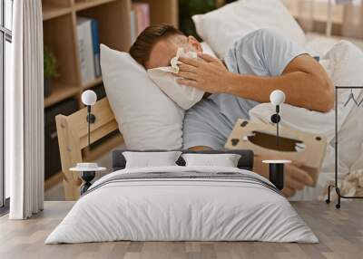 Crying hispanic man with a beard lying in bed at home, covering face with a tissue Wall mural