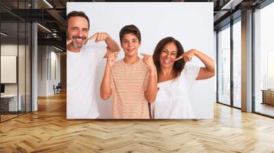 Family of three, mother, father and son standing over white isolated background smiling cheerful showing and pointing with fingers teeth and mouth. Dental health concept. Wall mural