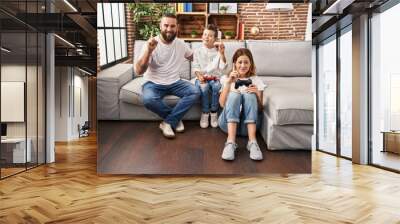 Family of three playing video game sitting on the sofa surprised with an idea or question pointing finger with happy face, number one Wall mural