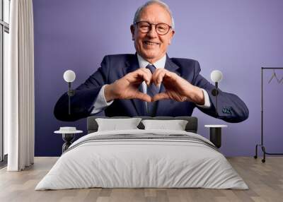 Grey haired senior business man wearing glasses and elegant suit and tie over purple background smiling in love doing heart symbol shape with hands. Romantic concept. Wall mural