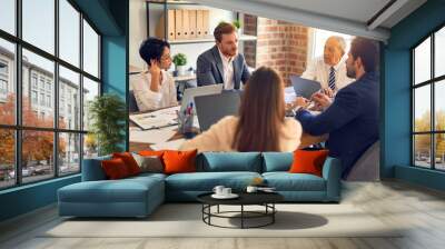 Group of business workers working together. Sitting on desk using laptop and talking at the office Wall mural