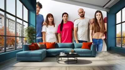 Group of young friends standing together over isolated background relaxed with serious expression on face. simple and natural looking at the camera. Wall mural