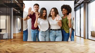 Group of young friends standing together over isolated background waiving saying hello happy and smiling, friendly welcome gesture Wall mural