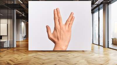 Hand of caucasian young man showing fingers over isolated white background greeting doing Vulcan salute, showing back of the hand and fingers, freak culture Wall mural