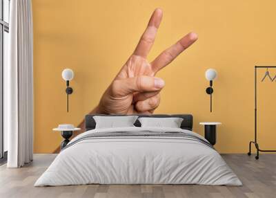 Hand of caucasian young man showing fingers over isolated yellow background counting number 2 showing two fingers, gesturing victory and winner symbol Wall mural