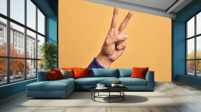 Hand of caucasian young man showing fingers over isolated yellow background counting number 2 showing two fingers, gesturing victory and winner symbol Wall mural