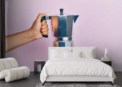 Hand of hispanic man holding coffee maker over isolated pink background. Wall mural