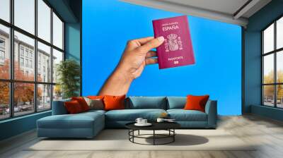 Hand of hispanic man holding spanish passport over isolated blue background. Wall mural