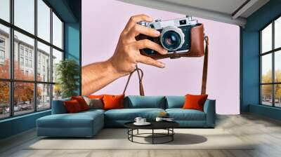 Hand of young hispanic man holding vintage camera over isolated pink background. Wall mural