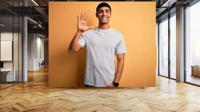 Handsome african american sportsman doing sport wearing sportswear over yellow background showing and pointing up with fingers number five while smiling confident and happy. Wall mural