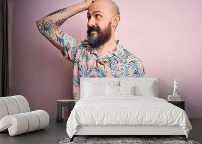 Handsome bald man with beard and tattoo wearing casual floral shirt over pink background smiling confident touching hair with hand up gesture, posing attractive and fashionable Wall mural