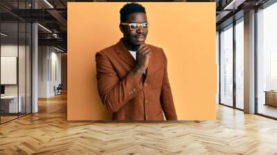 Handsome black man wearing elegant clothes and glasses smiling looking confident at the camera with crossed arms and hand on chin. thinking positive. Wall mural