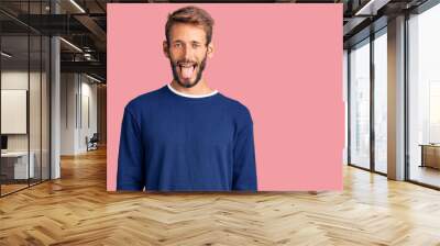 Handsome blond man with beard wearing casual sweater sticking tongue out happy with funny expression. emotion concept. Wall mural